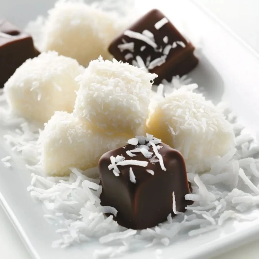 A Close Up Of Perfectly Formed Coconut Candies On A White Plate, Some Dipped In Glossy Chocolate, Surrounded By Shredded Coconut. Bright And Inviting Lighting.